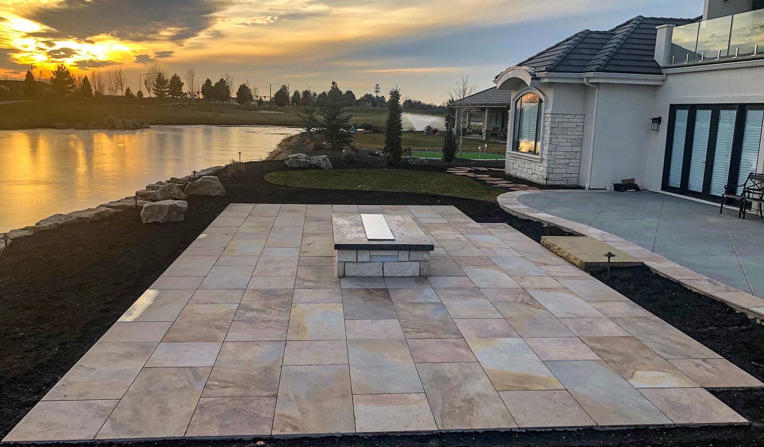 Paver gathering area and fire feature beside the water at sunset